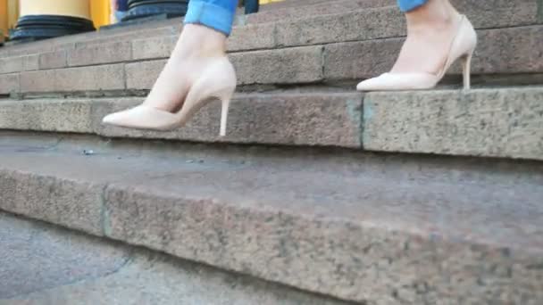 Ženské nohy v džínách a módní vysoké podpatky jdou dolů po schodech. Slim feet of attractive girl stepping on stairs irway. Mladá žena sestupuje po schodech. Dívka procházející se po ulici. Pomalý mo — Stock video