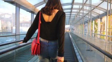 Yürüyen merdivende bavuluyla yürüyen tanınmayan genç bir kız. Seksi bir kadının bavulunu tekerlekli sandalyeyle çekmesi. Bayan tökezleyecek. Seyahat ya da tatil kavramı. Yavaş çekim Arka plan