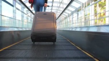 Yürüyen merdivende bavuluyla yürüyen tanınmayan genç bir kız. Seksi bir kadının bavulunu tekerlekli sandalyeyle çekmesi. Bayan tökezleyecek. Seyahat ya da tatil kavramı. Yavaş çekim Arka plan