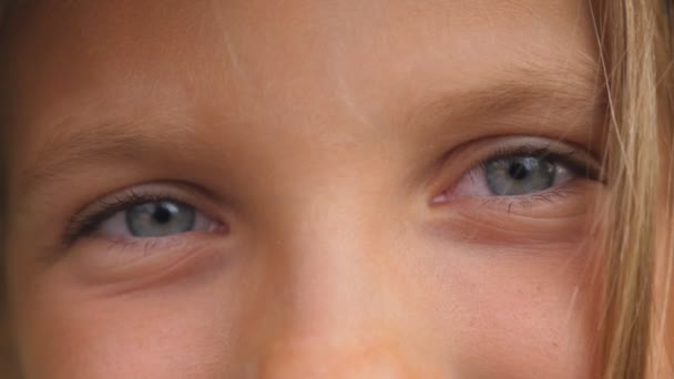 Detailní záběr modrých očí šťastné malé holčičky blikající a dívající se do kamery se šťastným pohledem. Portrét roztomilé tváře malého usmívajícího se dítěte s pozitivními emocemi. Pohled zepředu — Stock video