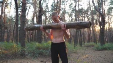 Kaslı adam ağır ağırlık antrenmanı kaslarını kaldırıyor. Dışarıda çalışan güçlü ve dayanıklı bir adam. Sporcu büyük kütükleri kullanarak doğada egzersiz yapıyor. Spor anlayışı ve aktif yaşam tarzı. Dolly vuruldu. Yaklaş.