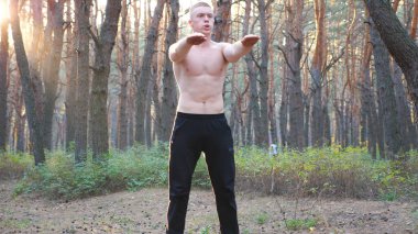 Genç adam güneşli bir ormanda çalışıyor. Sportif adam gün batımında çömelme hareketleri yapıyor. Doğada atlet eğitimi. Sağlıklı ve aktif yaşam tarzı kavramı. Dolly vuruldu. Yaklaş..