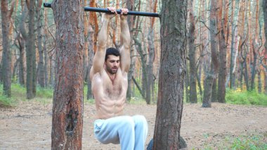 Atletik adam yatay çubukta karın egzersizi gösteriyor. Ormanda çalışan kaslı adam. Sporcu eğitimi açık havada. Spor anlayışı ve aktif yaşam tarzı. Yavaş çekim Dolly..