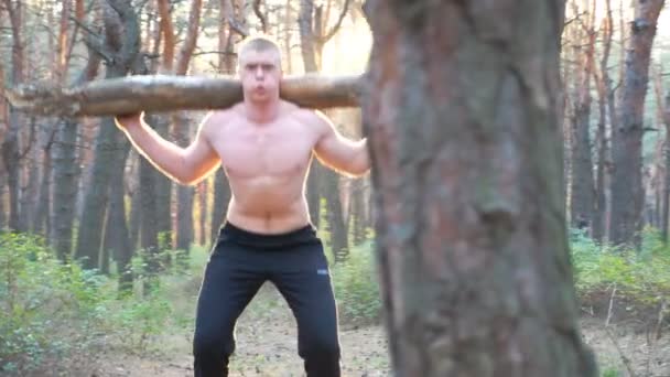 Een sportieve man die een groot blok hout vasthoudt. Sterke en stoere vent die aan het trainen is in het bos. Atletentraining in de natuur. Spiersportman tilt zwaar gewicht op. Sportieve en actieve levensstijl. Dolly schot — Stockvideo