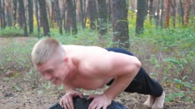 Ormanda şınav çeken güçlü bir adam. Erkek sporcu doğada egzersiz yapıyor. Genç adam dışarıda antrenman yapıyor. Kas sporcusu sıkı ve yoğun idman yapıyor. Spor anlayışı ve aktif yaşam tarzı. Kapat.