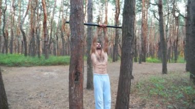 Atletik adam karın kaslarını çalıştırıyor yatay çıtada vücut kaldırıyor. Ormanda çalışan kaslı adam. Sporcu dışarıda jimnastik egzersizleri yapıyor. Spor ve aktif yaşam tarzı kavramı