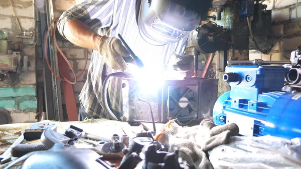 Repairer welding some detail of auto. Mechanic working in garage or workshop with welding machine and other professional equipment. Welder using protective mask from flashes. Slow motion Dolly shot.