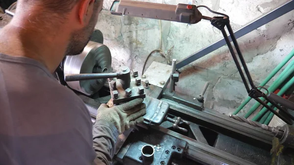 Unrecognizable man working with old workbench in his garage or workshop. Mechanic using lathe for metal processing. View on turning work. Slow motion Top view.