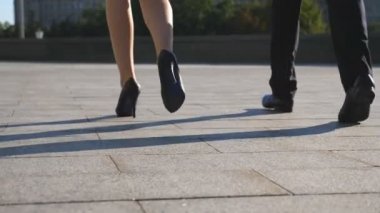 Ayakları iş adamı ve yüksek topuklu ayakkabılı bir kadın şehir caddesinde yürüyor. İş adamı ve iş kadını birlikte işe gidip geliyorlar. Bacaklar işe koyuluyor. Meslektaşlar dışarı çıkıyor. Yavaş çekim. Yakın çekim.