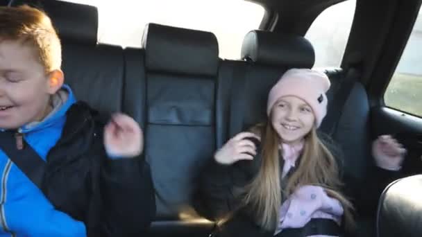 Ευτυχισμένο μικρό αγόρι και κορίτσι χορεύει στο αγαπημένο τους τραγούδι, ενώ κάθεται σε ένα πίσω κάθισμα του αυτοκινήτου εν κινήσει. Δύο μικρά παιδιά ακούνε ραδιόφωνο και απολαμβάνουν τη μουσική ενώ ταξιδεύουν οδικώς. Έννοια του ταξιδιού. Αργή κίνηση — Αρχείο Βίντεο