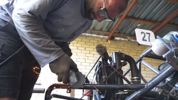 Volwassen reparateur of monteur slijpen metaal met behulp van cirkelzaag. Werknemer snijden een aantal auto detail in de garage of werkplaats. Auto master zet onderhoudsauto aan. Warme vonken vliegen rond. Zijaanzicht — Stockvideo