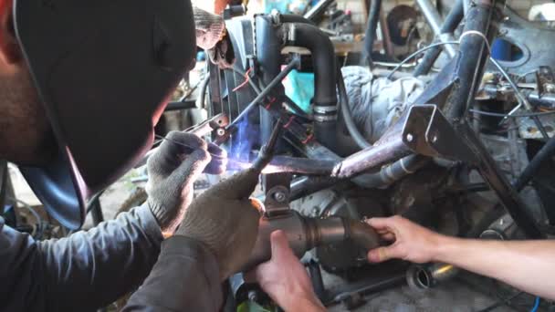 Mechaniker in Schutzmaske schweißt Autodetails zusammen. Reparaturwerkstätten reparieren automatisch. Männer, die in einer Garage mit Schweißgerät und anderen Geräten arbeiten. Automechaniker engagieren sich bei der Wartung von Autos. Nahaufnahme Zeitlupe — Stockvideo