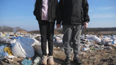 Küçük bir kız ve oğlanın portresi, arka plandaki çöplüğe bakıyor. Küçük ciddi çocuklar çöp sahasında durup el ele tutuşuyorlar. Çevre kirliliği. Turna atışı