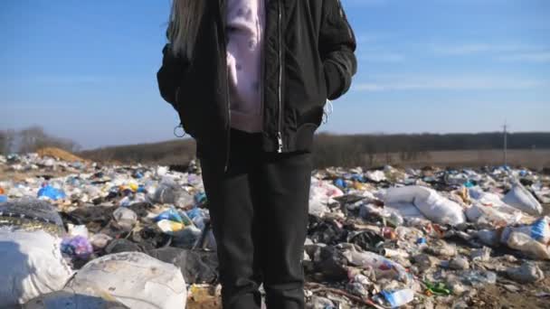 田舎の埋め立て地に立つ悲しい少女の肖像画。小さな女性の子供のカメラに汚れたゴミダンプのぼやけた背景に見えます。環境汚染問題。クレーンショット — ストック動画