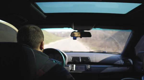 View from backseat on young man drives a car on empty road. Guy rides in his modern SUV through countryside. Male tourist travels on his auto. Concept of journey. Close up Slow motion.