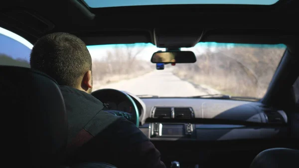 View from backseat on young man drives a car on empty road. Guy rides in his modern SUV through countryside. Male tourist travels on his auto. Concept of journey. Close up Slow motion.