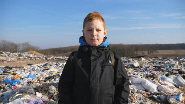 这个严肃的小男孩的画像矗立在乡间的垃圾堆里 小男孩在垃圾堆模糊的背景下看着摄像机 环境污染问题 — 图库照片