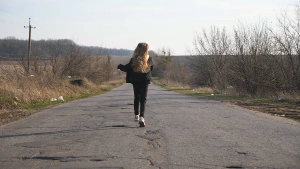 穿着夹克的小女孩在空荡荡的路上走来走去 在阳光灿烂的日子里跳舞 一个金发碧眼的小女孩在乡间空旷的车道上玩乐 慢动作 — 图库照片