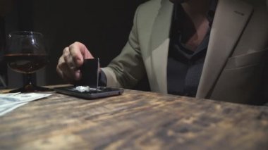 Kredi kartı tutan ve akıllı telefondan kokain üreten bağımlıların erkek elini kapat. Uyuşturucu satıcısı telefon ekranından 100 dolarlık banknotlar yollamış. Düşük açı görünümü