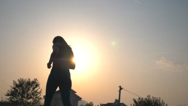 Aktives Mädchen beim Joggen entlang der Landstraße mit Sonnenuntergang im Hintergrund. Junge, sportliche Frau, die abends im Freien trainiert. Sportlerin beim Lauftraining. Konzept eines gesunden Lebensstils. Rückseite