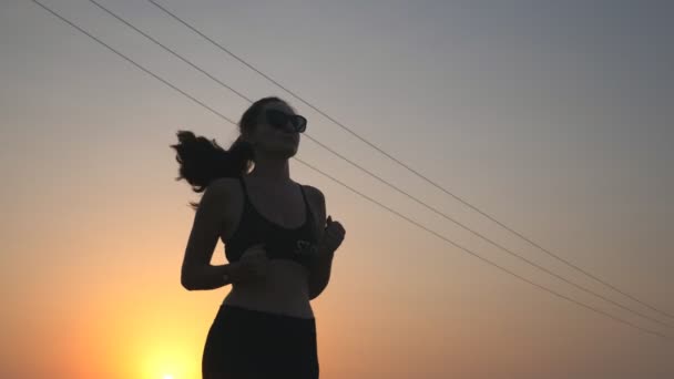 Aktivní štíhlé dívka jogging na venkovské silnici s večerní oblohou na pozadí. Sportovkyně na běžeckém tréninku. Mladá sportovní žena cvičí venku při západu slunce. Zdravý aktivní životní styl. Nízký pohled — Stock video