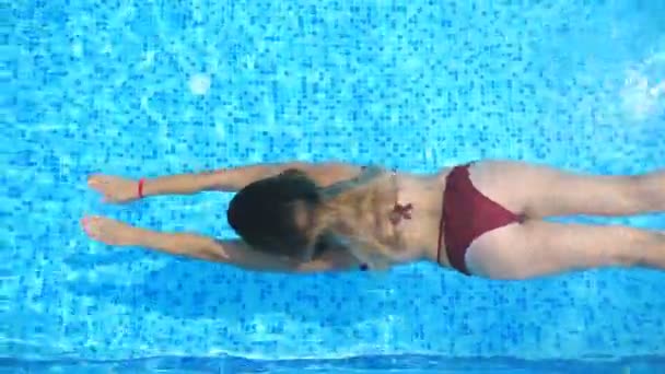 Mladá žena v červených bikinách plavající pod vodou v bazénu s křišťálově čistou vodou. Sexy dívka osvěžující v povodí hotelu. Elegantní dáma odpočívá na tropickém letovisku během dovolené. Zpomalit pohled shora — Stock video