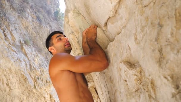 젊은 근육질의 남자가 바위 위를 조심스럽게 등반 합니다. 암벽 봉우리에 오르는 강한 남자는 많은 노력을 기울입니다. 산악인 이 산 정상으로 가고 있어. 극단적 인 스포츠 또는 활동적 인 생활 방식의 개념. 느린 동작 — 비디오