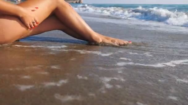 Pernas finas de mulher deitada na praia tropical e desfrutando de férias. Ondas quentes do oceano lavando pés femininos bronzeados. Menina relaxante na beira-mar com paisagem marinha no fundo. Conceito de férias de verão. Dolly atirou — Vídeo de Stock