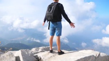 Sırt çantalı gezgin dağ yamacında duruyor ve elini kaldırıyor özgürlüğün tadını çıkarıyor. Seyahat sırasında yeni yerler keşfetmek için dinlenen bir adam. Tepedeki manzaraya hayran turistler. Arka plan