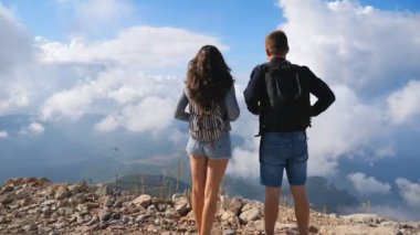Sırt çantalı birkaç yürüyüşçü dağ yamacında dikilip manzaranın tadını çıkarıyorlar. Erkek ve kadın birlikte yeni yerler keşfetmek için aktif olarak dinleniyorlar. Güzel arka plan. Dolly çekim Arka plan
