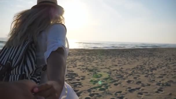 Девушка в пляжной одежде держит мужчину за руку и бежит к океану на закате. Следуйте за мной снимок женщины с рюкзаком, ведущей своего парня на берег моря. Концепция летних каникул или каникул. Медленное движение POV — стоковое видео