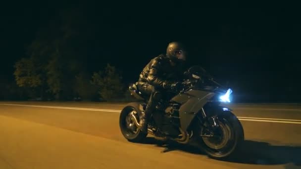 Młody człowiek w kasku szybko jeździ na nowoczesnym, czarnym motocyklu sportowym na wieczornej ulicy miasta. Motocyklista ściga się na motocyklu nocą po pustej drodze. Facet jeździ na rowerze. Pojęcie wolności i hobby. Zamknij się. — Wideo stockowe
