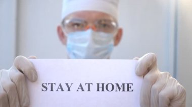 Sıhhiyeci kendini izole etmeye meyilli bir poster gösteriyor. Erkek doktor, Coronavirus salgını sırasında evde duran bir resim tutuyor. COVID-19 salgınından korunma kavramı