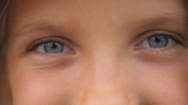 Close-up van blauwe ogen van gelukkig klein meisje knipperen en kijken in de camera met een gelukkig gezicht. Portret van een schattig gezicht van een lachend kind dat met positieve emotie toekijkt. Vooraanzicht — Stockvideo