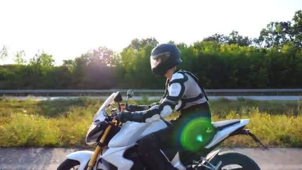 Muž v helmě řízení silný sportovní motocykl podél dálnice. Motorkář jezdí na motorce po venkovské silnici. Mladý muž si užívá rychlost za slunečného dne. Koncept svobody. Pomalý pohyb Boční pohled