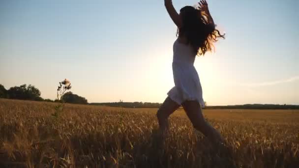 Mulher irreconhecível em vestido branco correndo pelo campo com trigo amarelo ao pôr do sol. Menina despreocupada jovem desfrutando de liberdade em belo ambiente da natureza. Paisagem de verão cênica. Vista lateral Fechar — Vídeo de Stock