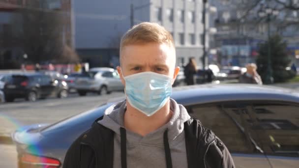 Egy fickó, aki védőmaszkot visel a kinti vírusoktól a tömegben. A városi utcában áll egy arcmaszkos fiatalember portréja. Az egészségi és biztonsági élet koncepciója a coronavirus pandémiától — Stock videók
