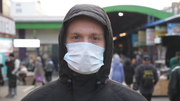 Retrato de jovem com máscara facial médica fica na rua da cidade. Um tipo a usar máscara protectora do vírus ao ar livre no meio da multidão. Conceito de saúde e segurança da pandemia de coronavírus — Vídeo de Stock