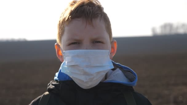 Retrato de menino com máscara facial médica em pé ao ar livre. Criança masculina triste usando máscara protetora do vírus fora. Conceito de saúde e segurança vida de coronavírus e pandemia. Fechar — Vídeo de Stock