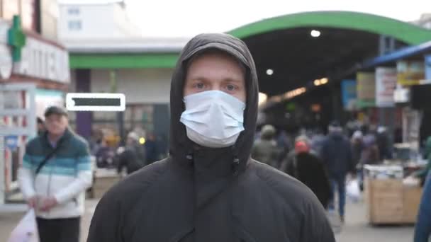 Retrato de jovem com máscara facial médica fica na rua da cidade. Um tipo a usar máscara protectora do vírus ao ar livre no meio da multidão. Conceito de vida de saúde e segurança contra coronavírus e pandemia — Vídeo de Stock