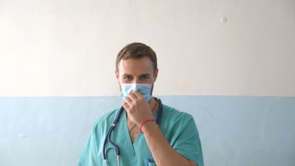 Retrato de un joven médico quitarse la mascarilla médica y sonreír. Trabajador médico quitando la máscara protectora y mirando con emoción positiva. Concepto de vida segura frente al coronavirus y la pandemia. COVID-19 — Vídeos de Stock