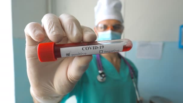 Молодой доктор показывает пробирку с образцом крови коронавирусу COVID-19. Медик в защитных перчатках хранит образцы крови в больнице или лаборатории. Концепция здоровья и безопасности жизни от пандемии — стоковое видео
