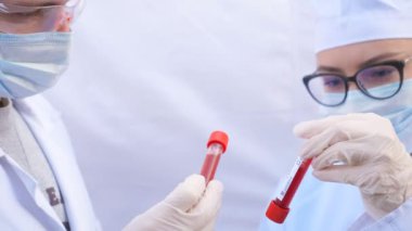 İki doktor koronavirüs için kan örnekleriyle test tüplerini inceliyor. Koruyucu eldivenli erkek ve kadın sağlık görevlileri kan örneklerini test ediyor. COVID-19 salgınından sağlık ve güvenlik hayatı kavramı