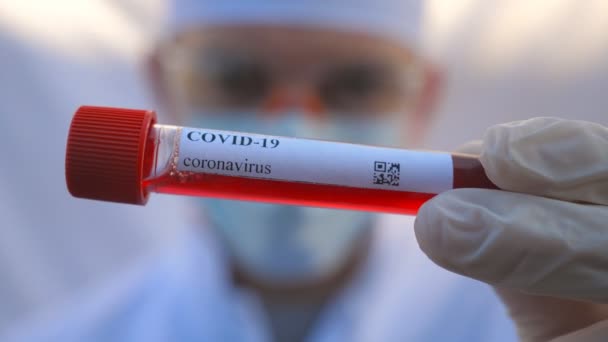 Mano del médico con guantes protectores analizando la muestra de sangre al virus COVID-19. Brazo del médico sosteniendo el tubo de ensayo con muestra de sangre al coronavirus. Concepto de la vida de salud y seguridad de la pandemia. De cerca. — Vídeo de stock