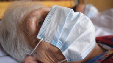 Virüsten koruyucu maske takan büyükannenin portresi. Hastanede yatarken kameraya bakan üzgün bakışlı hasta kadın. Coronavirus 'tan sağlık ve güvenlik hayatı kavramı. Kapat.
