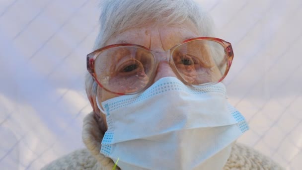 Portrét babičky s ochrannou maskou z viru. Starší dáma se dívá do kamery a ukazuje smutné emoce. Koncept zdraví a bezpečnosti života před pandemií. Karanténa koronaviru pro starší osoby — Stock video