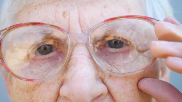 Детальный портрет бабушки в очках с задумчивым зрением. Закрыть морщинистое лицо пенсионерки, смотрящей в камеру и регулирующей очки. Грустное выражение лица бабушки. Медленное движение — стоковое видео