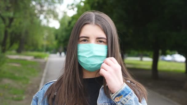 Retrato de mulher jovem feliz tira máscara facial médica e sorrindo. Menina remove máscara protetora do vírus COVID-19 ao ar livre. Conceito de saúde e segurança da pandemia de coronavírus. Fechar — Vídeo de Stock