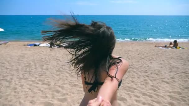 Красива дівчина тримає чоловічу руку і бігає на курортному пляжі до океану. Слідом за мною стріляє молода жінка, тягне свого хлопця на морський берег. Літні канікули або відпустка. Точка зору POV Повільний рух — стокове відео
