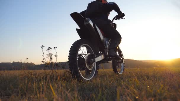 Rad des Motocross-Motorrads, das ins Schleudern gerät und Boden oder Schmutz aufwirbelt. Motorrad zu Beginn der Bewegung. Motorradfahren bei Sonnenuntergang. Schöne Landschaft im Hintergrund. Zeitlupe Nahaufnahme — Stockvideo